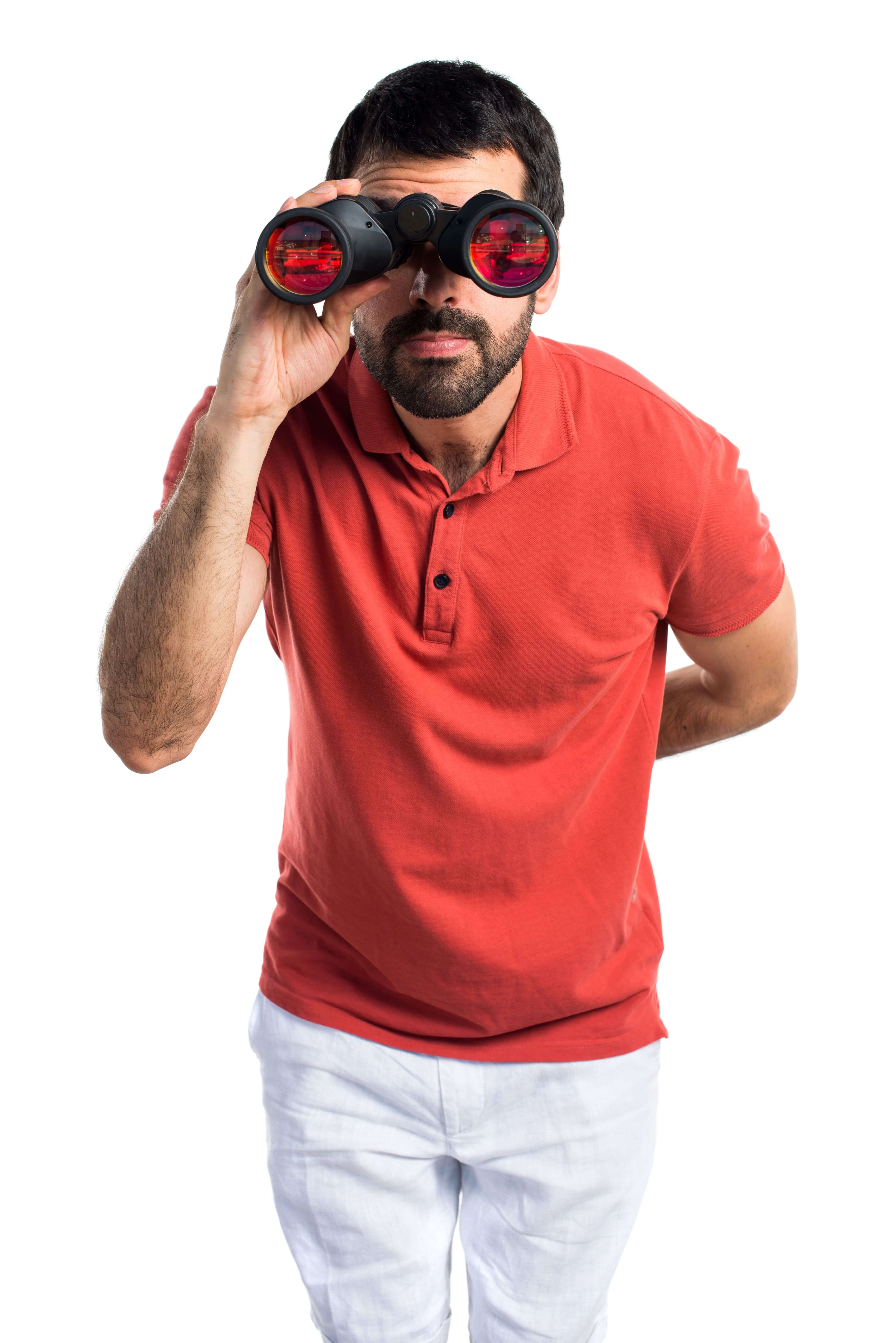 A man in a red shirt uses binoculars to view something in the distance.