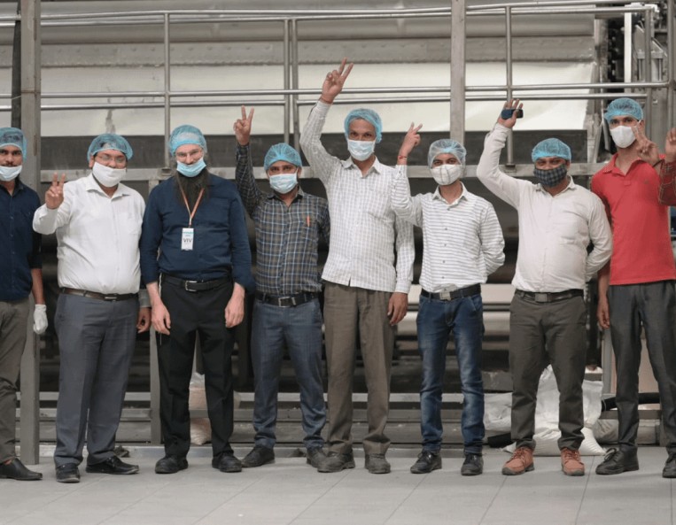 A group of masked men standing in front of a machine at the Goodrich Potato Factory, some of them showing the victory V sign.
