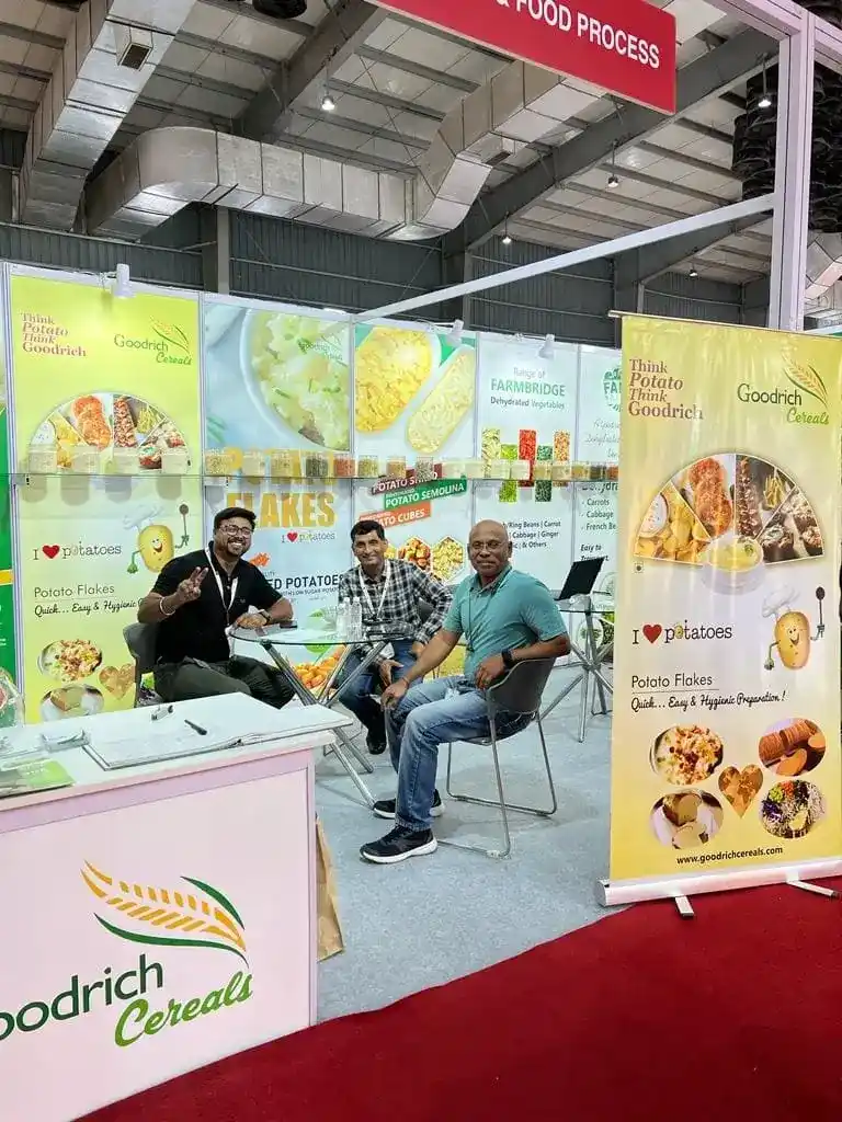 Three men seated at a table in the Goodrich Exhibition Anuga Mumbai, showcasing a food and beverage expo.