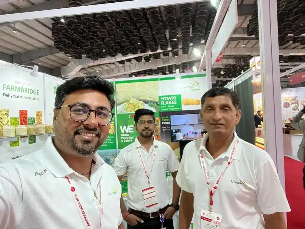 Three men in white shirts standing in front of a booth at the Goodrich exhibition Anuga Mumbai.